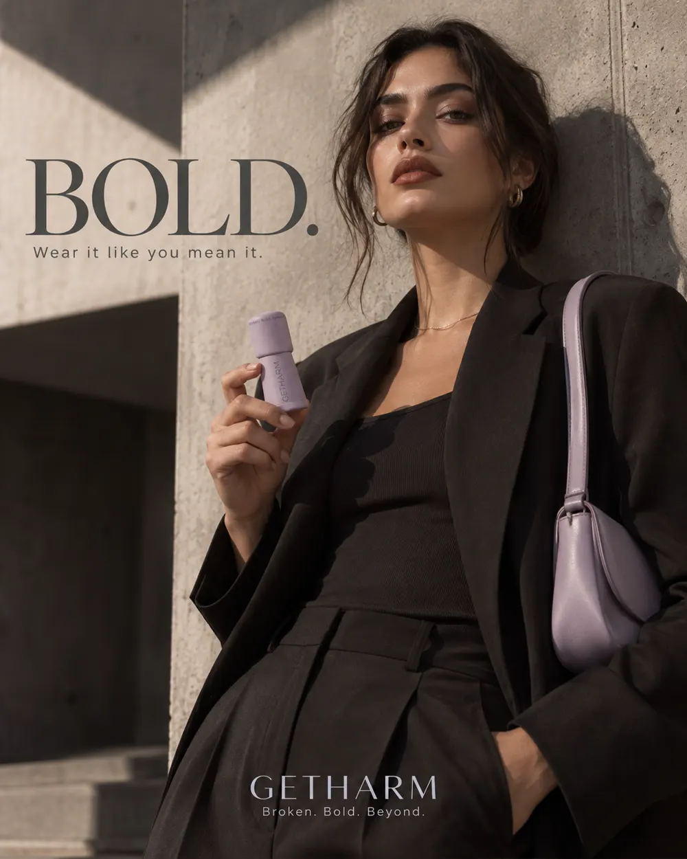 GETHARM campaign image: model in black tailoring against concrete, holding MatteLip