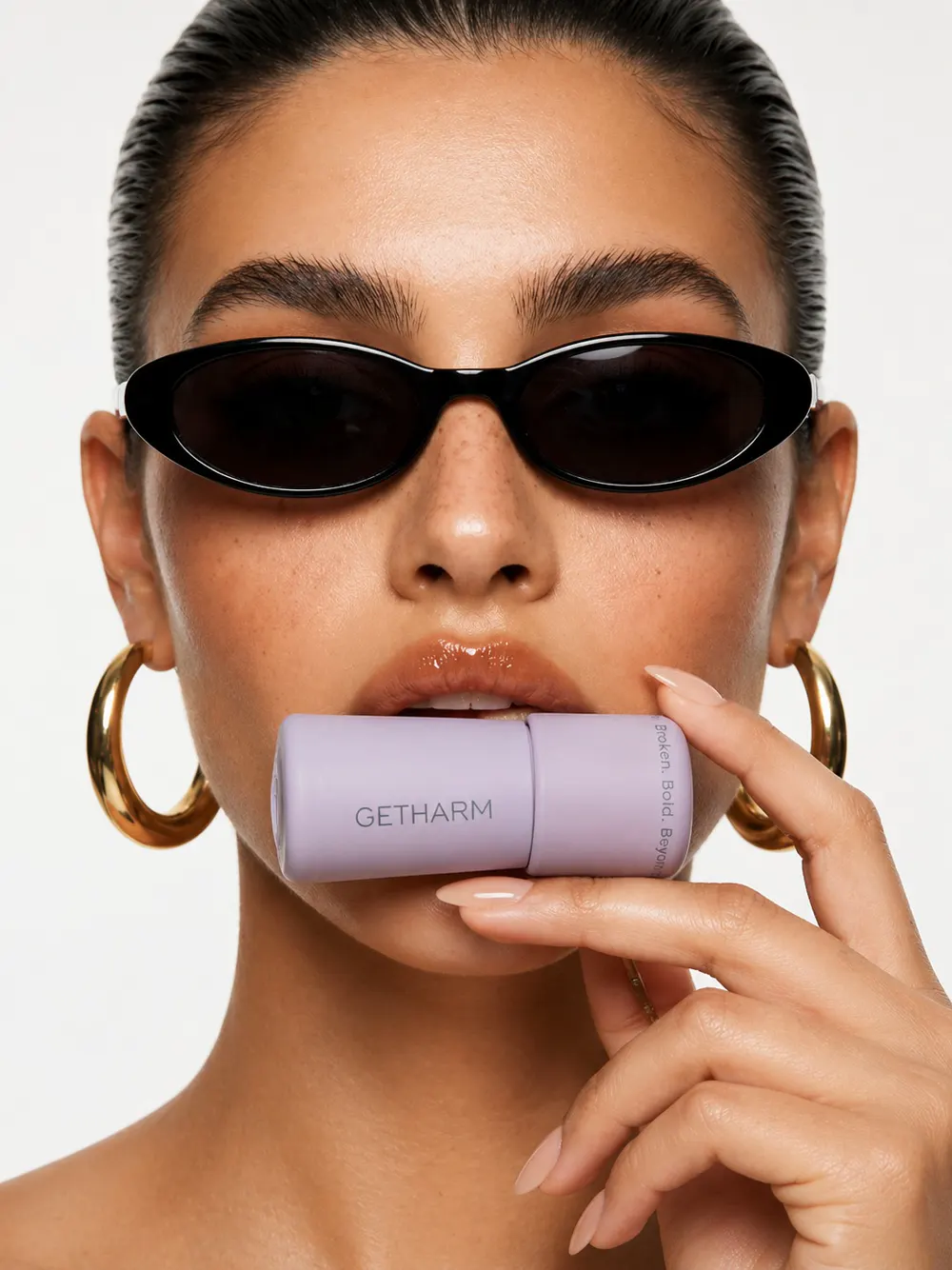 Model in dark sunglasses and gold hoops holding MatteLip to her lips
